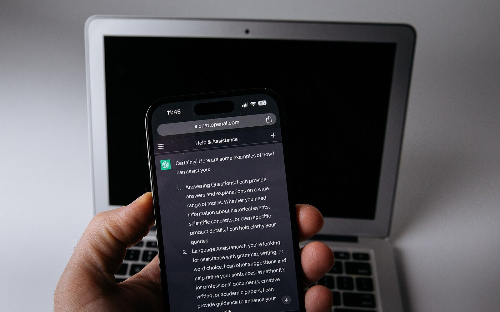 Əldə tutulan smartfonda AI çat tətbiqi, arxa planda noutbuk